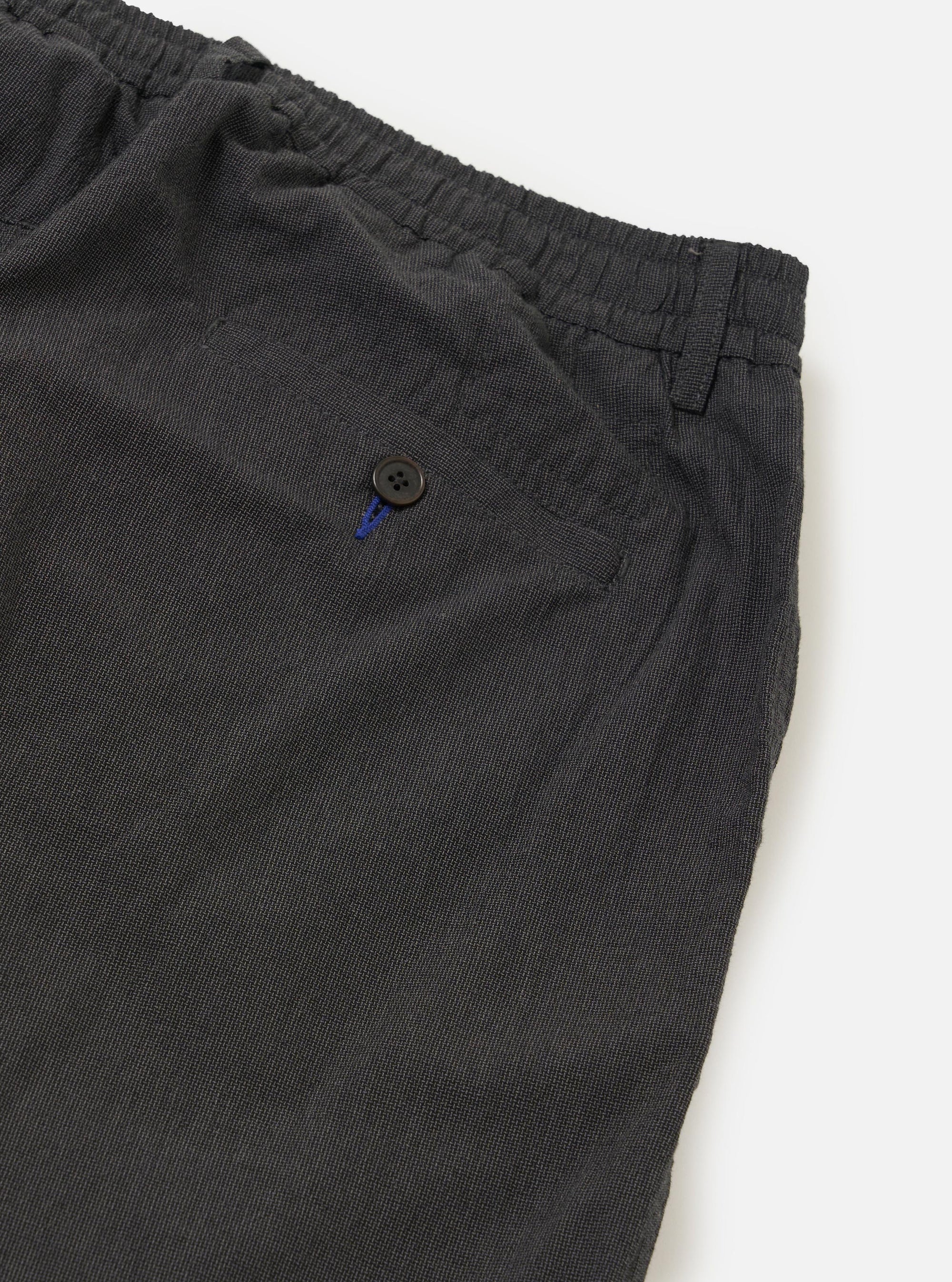 A close-up view of the back of the Charcoal Seattle Cotton Pleated Track Pant focuses on the waistband and two rear pockets. One pocket is a buttoned jetted style, while the other features a buttoned flap. The charcoal grey cotton fabric is shown against a plain white background.