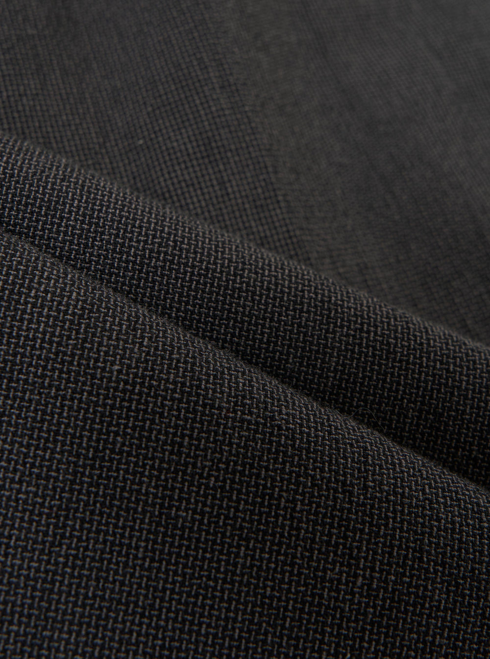 A detailed, close-up fabric swatch of the charcoal grey Seattle cotton material used for the Pleated Track Pant. The image highlights the fine basket weave and textured surface of the cotton fabric.