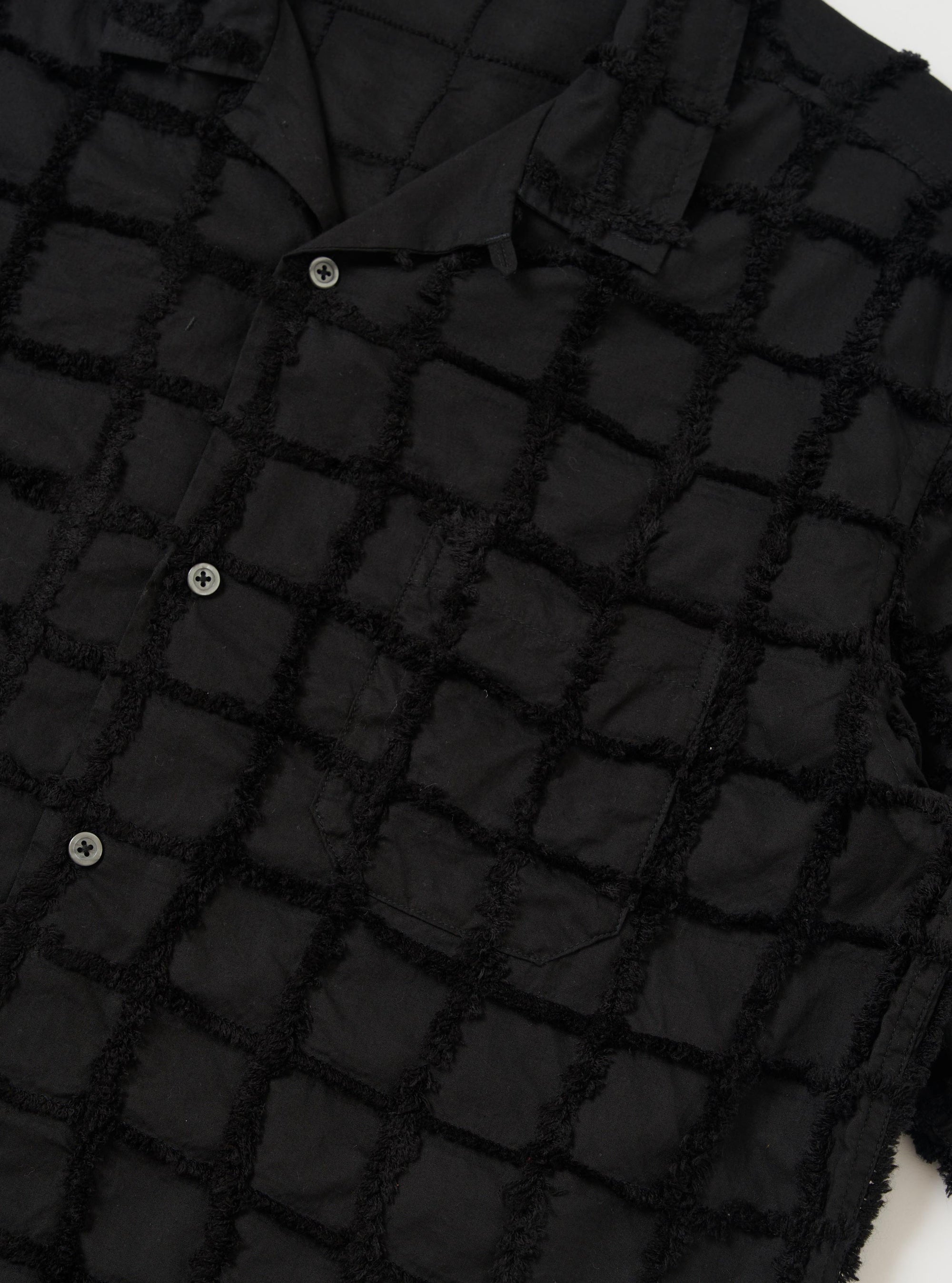 The Black 3D Check Road Shirt is shown from a rear perspective, laid flat against a solid white background. The image highlights the short sleeves, straight hem, and the unique textured, tufted surface of the black 3D check cotton fabric.