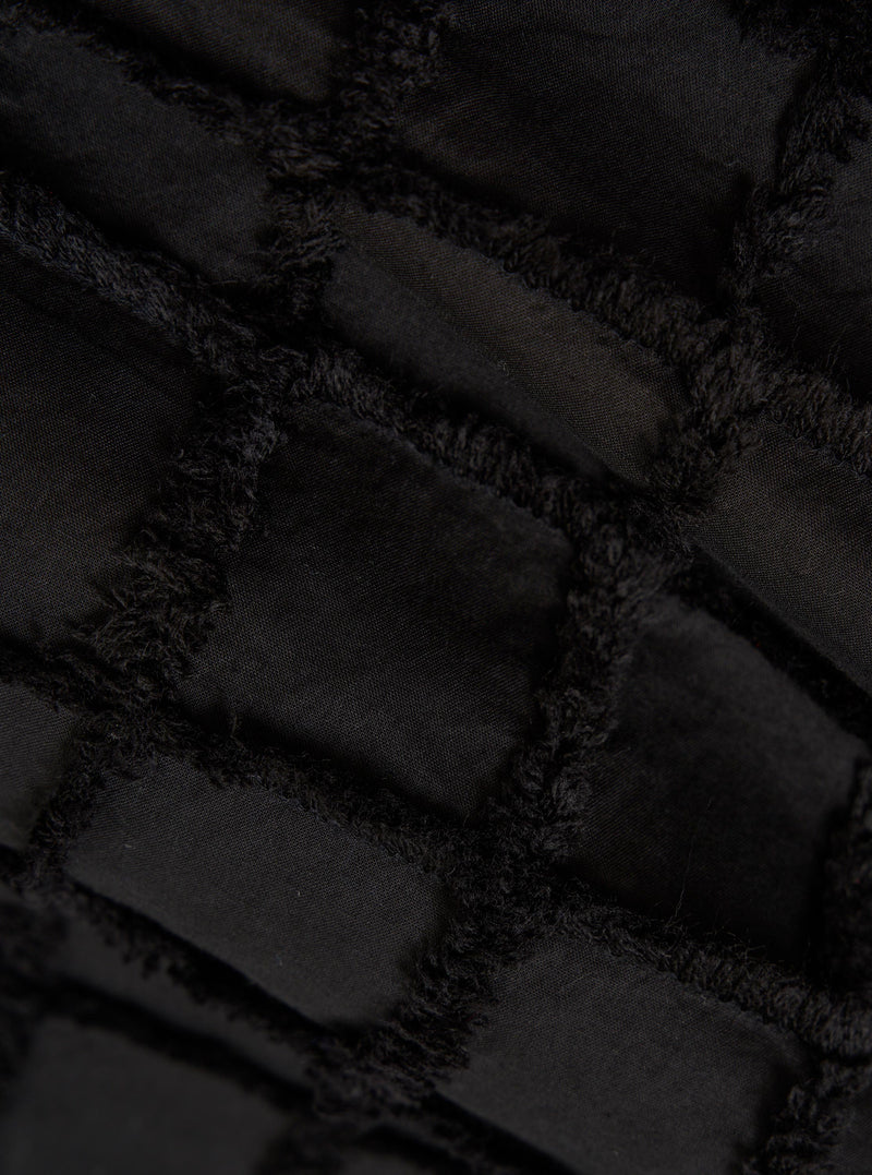 A detailed, close-up fabric swatch of the Black 3D Check Windcheater Jacket highlights a textured cotton material with a three-dimensional grid or checkered pattern in black and dark grey. The image focuses solely on the intricate weave and tonal contrast of the fabric.