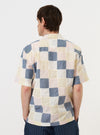 A model wears the Pastel Check Patchwork Camp Shirt against a plain white background. The shirt features a multi-colored patchwork design with various pastel check patterns and a relaxed camp collar. The image captures the model from the waist up, showcasing the short-sleeved construction and the textured detail of the cotton patchwork fabric.