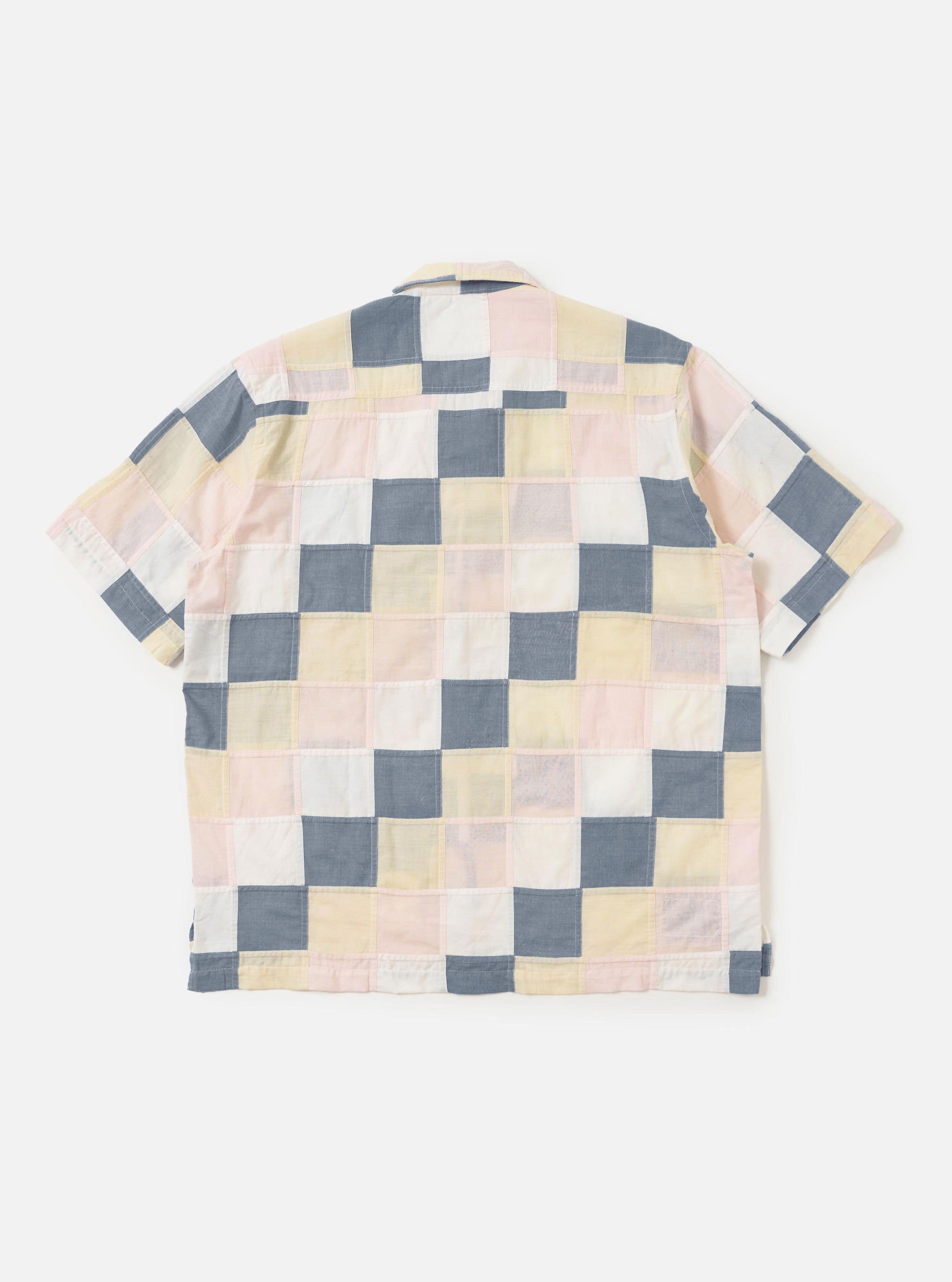 The back of the Pastel Check Patchwork Camp Shirt is shown laid flat against a plain white background. The garment features a patchwork construction of various pastel checked patterns in blue, navy, and ecru. Prominent details include the short sleeves, a straight hem, and a horizontal back yoke.