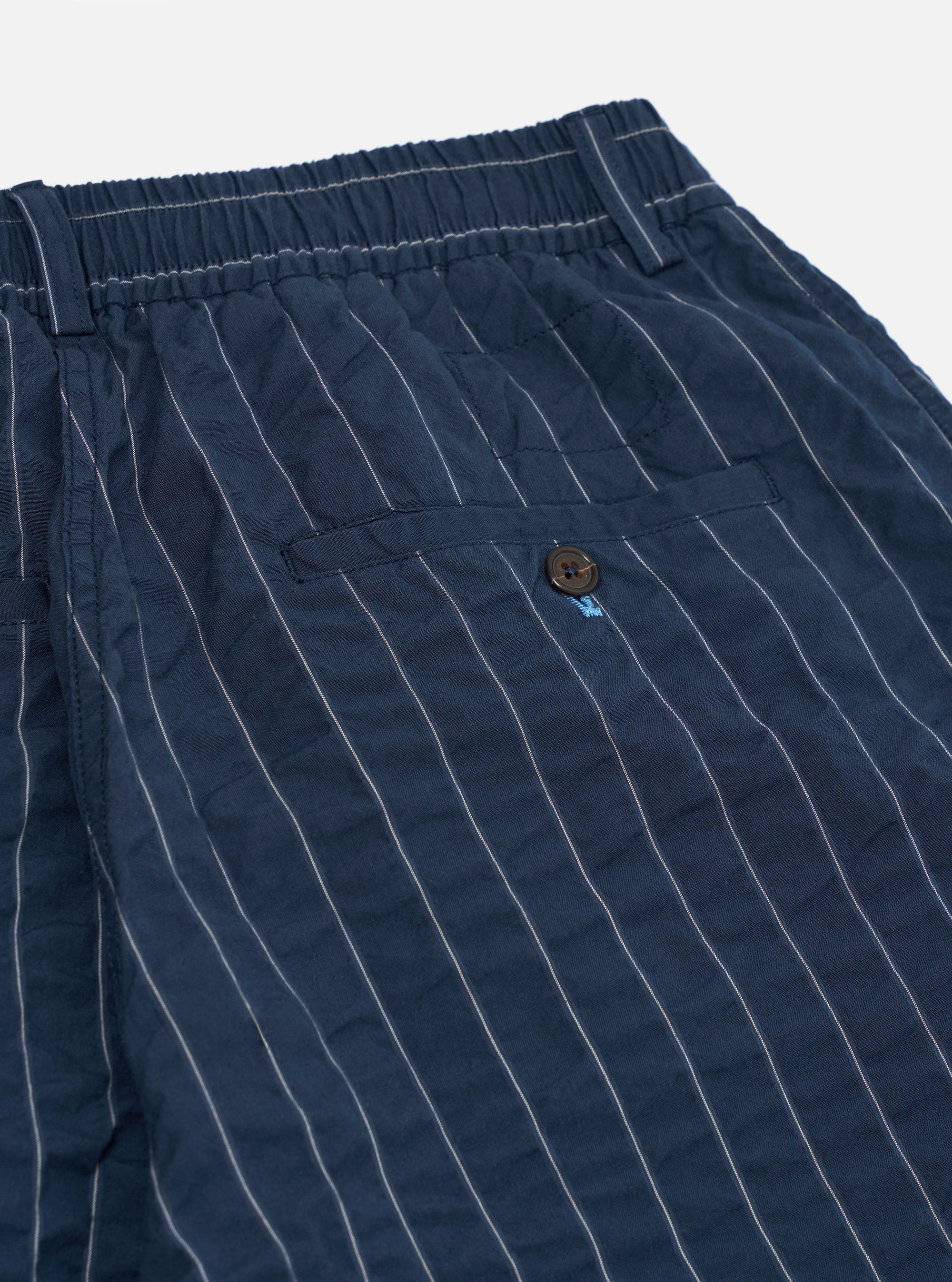 A pair of Navy Chester Stripe Oxford Pants is shown from the back, laid flat against a plain white background. The image highlights the two rear pockets, one a buttoned flap and the other a buttoned jetted pocket, as well as the elasticated drawstring waistband.