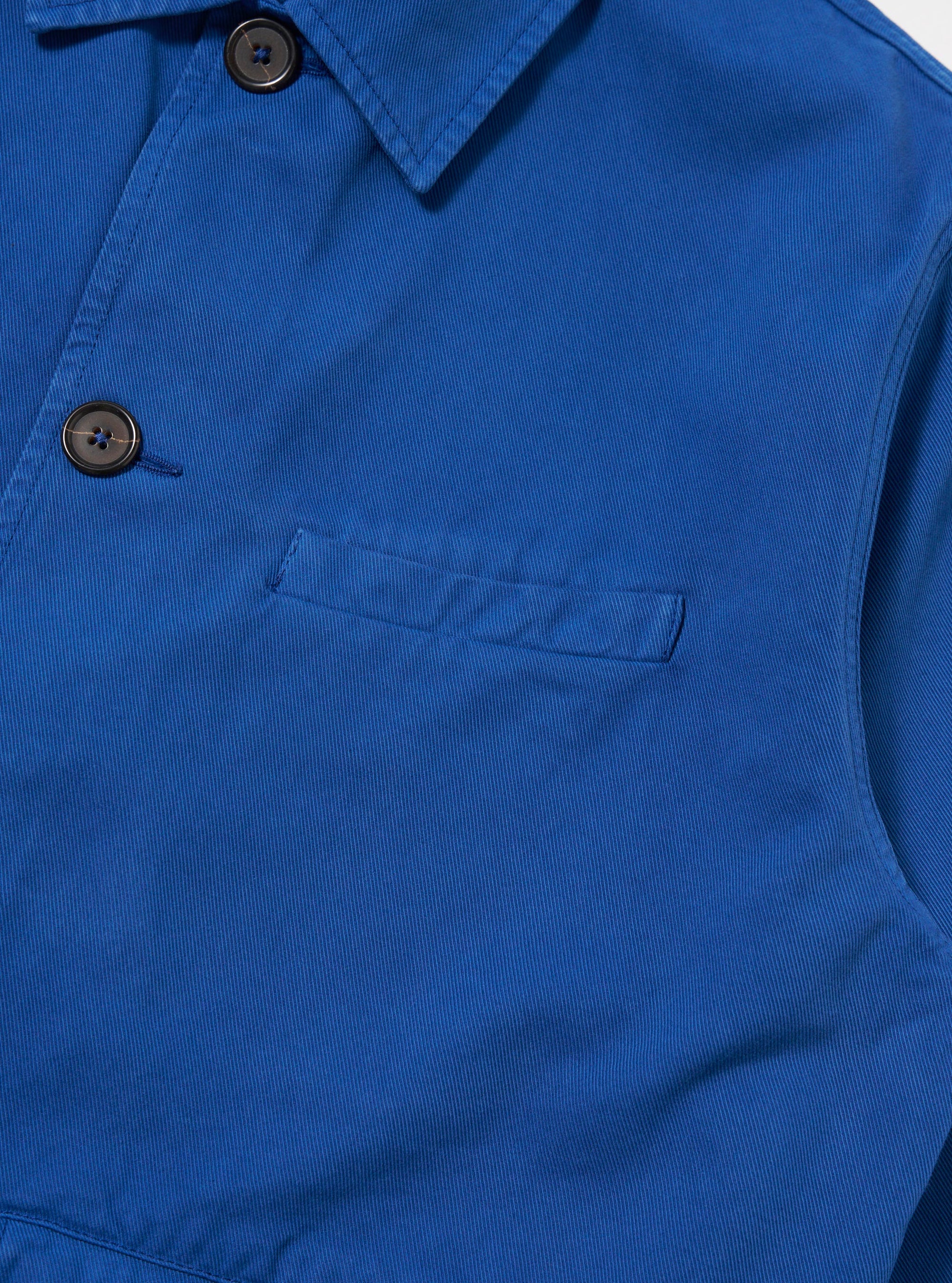Close-up of the Paraboot x Universal Works Navy Derek Twill Warmus Jacket. Shows the blue twill fabric, brown buttons, and pocket detail against a plain white background.
