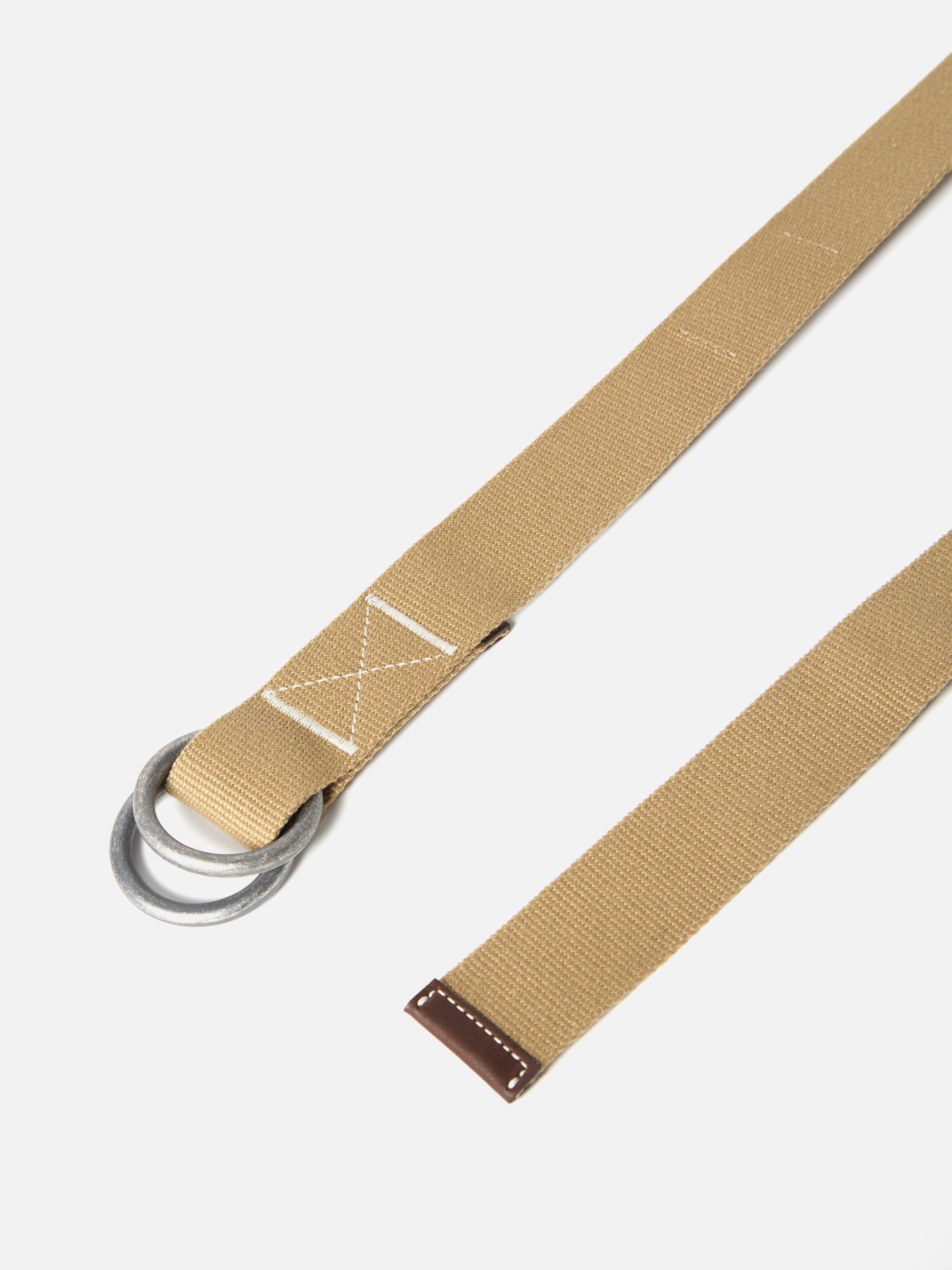 Close-up of a Sand Canvas O Ring Belt on a white background. The belt is made of canvas with a sand color and has an O-ring buckle. The end of the belt has a brown leather tip.