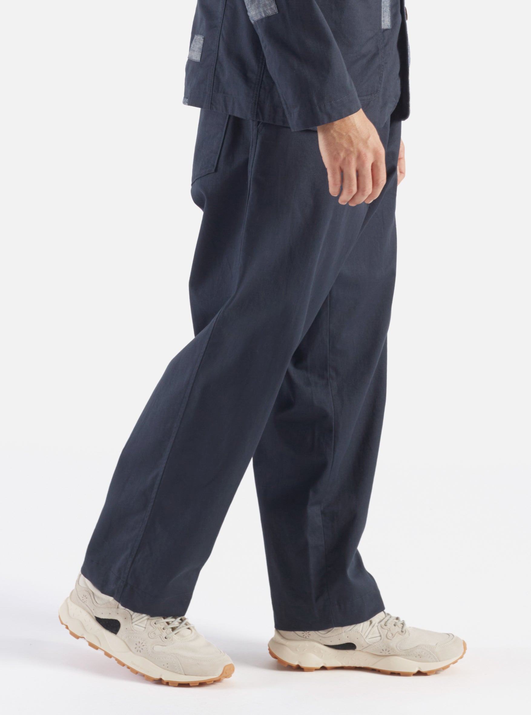 A model walks in a studio setting wearing the Navy Twill Duke Pant. The pants are navy and made of twill. The background is a bright white.