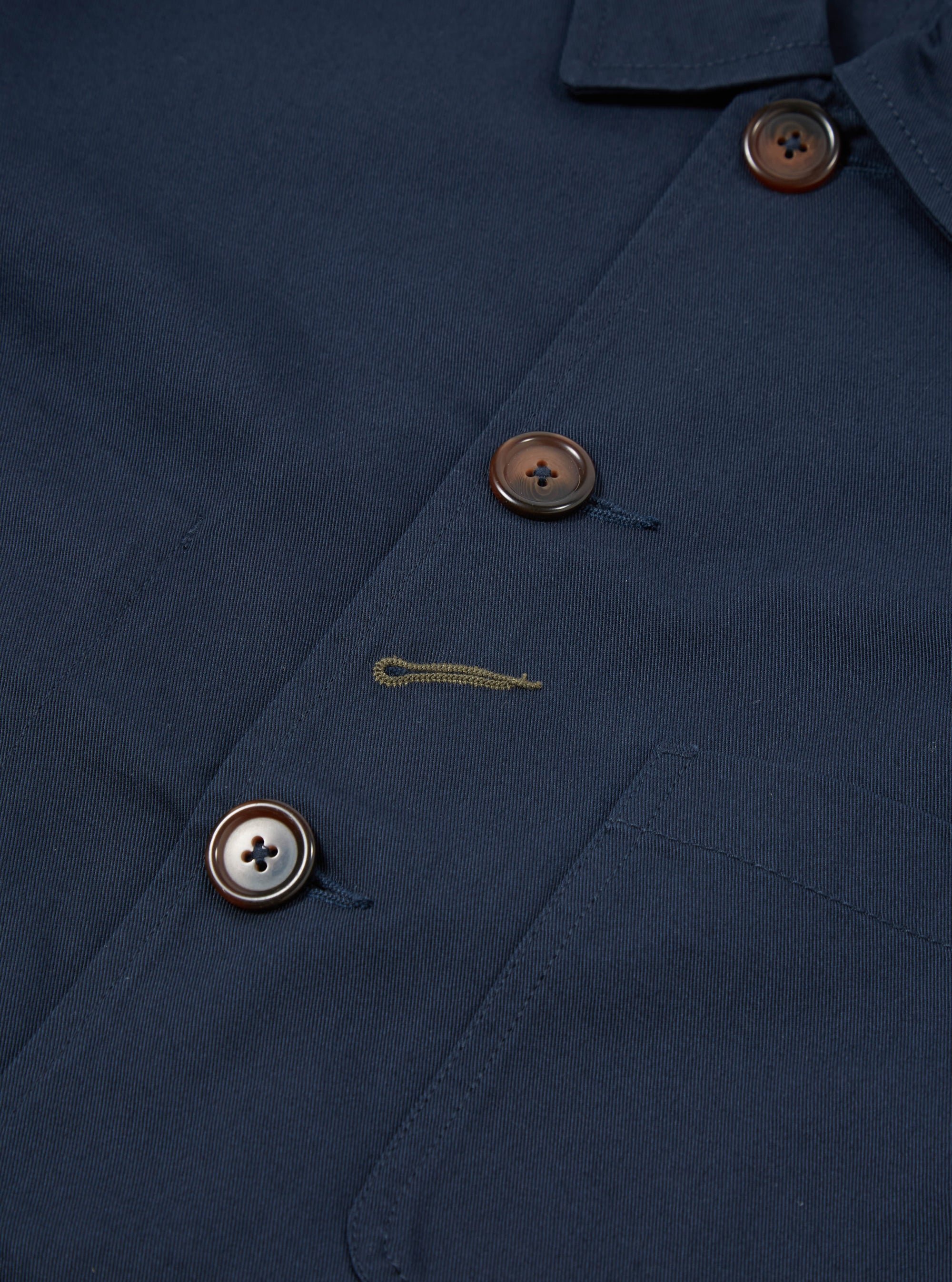 Close-up of the navy twill Bakers Jacket, showcasing the fabric texture, button details, and pocket stitching. The jacket is neatly arranged on a flat surface.