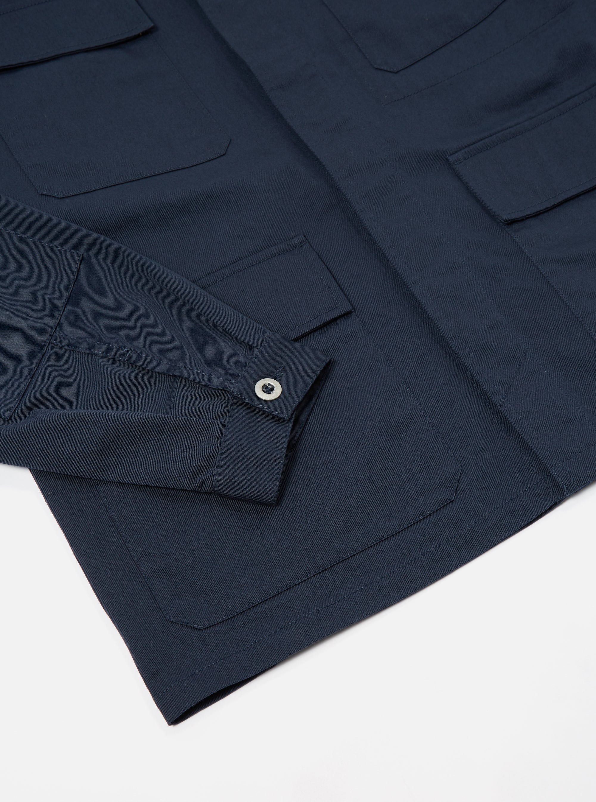 Close-up of the Navy Twill MW Fatigue Jacket on a white surface. The jacket features a buttoned sleeve and multiple pockets.