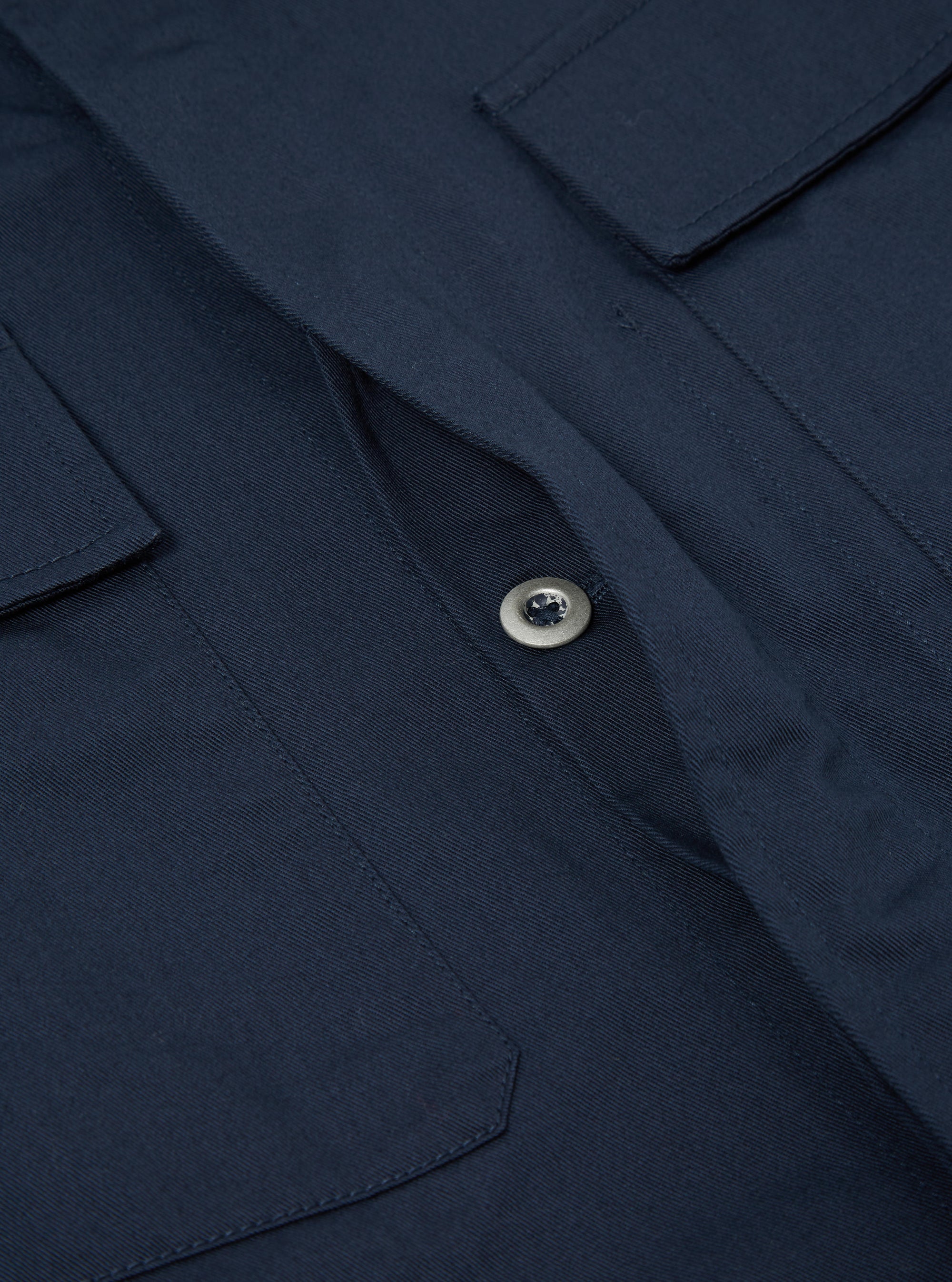 Close-up of the Navy Twill MW Fatigue Jacket showing the twill fabric, button, and pocket details. The jacket is laid flat on a neutral surface.
