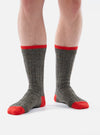 Close-up of a person wearing the Derby Wool Hike Sock, which is gray with red accents on the toe and top. The socks are ribbed and made of wool, against a white background.