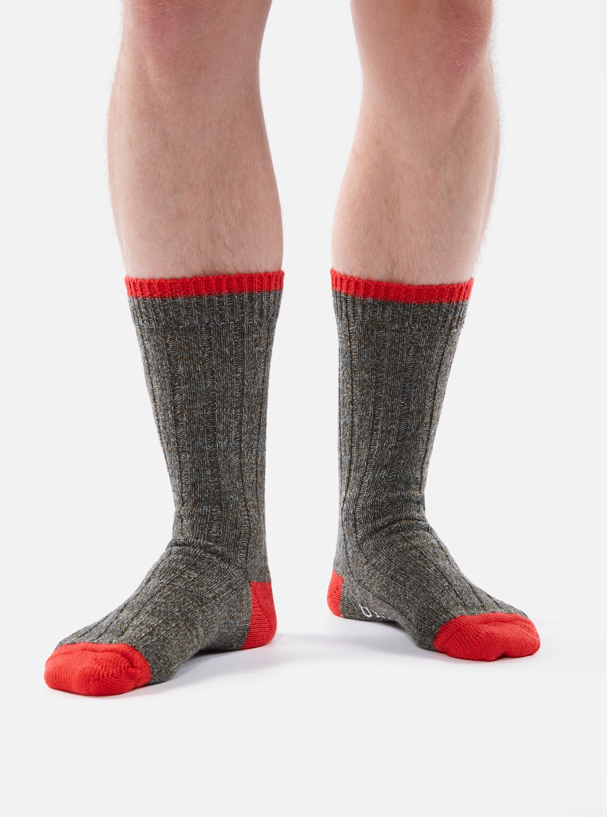 Close-up of a person wearing the Derby Wool Hike Sock, which is gray with red accents on the toe and top. The socks are ribbed and made of wool, against a white background.