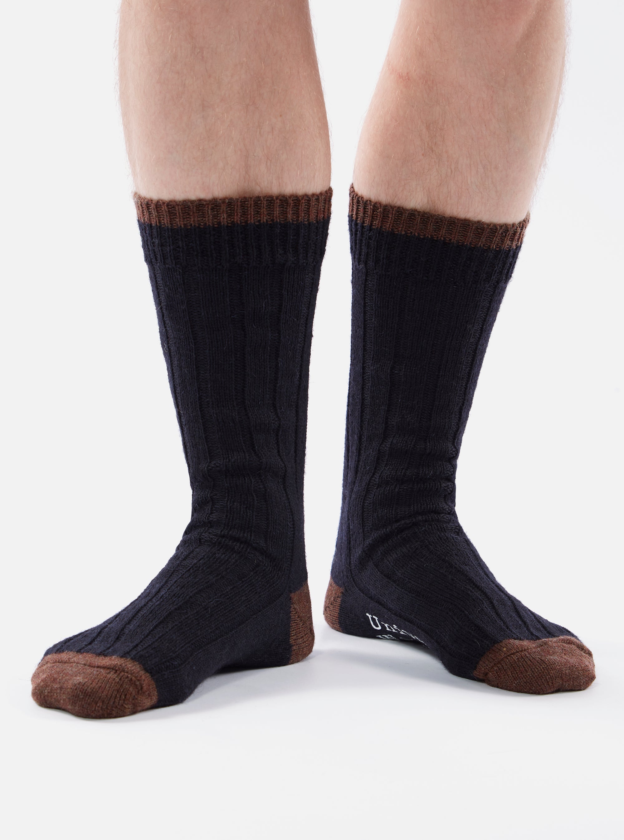 Close up of a person wearing Navy Wool Hike Sock. The socks are navy blue with brown toes and cuffs. The background is white.