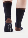 Close-up of a person wearing Navy Wool Hike Sock. The socks are navy with brown accents on the heel and cuff. The background is a bright white.