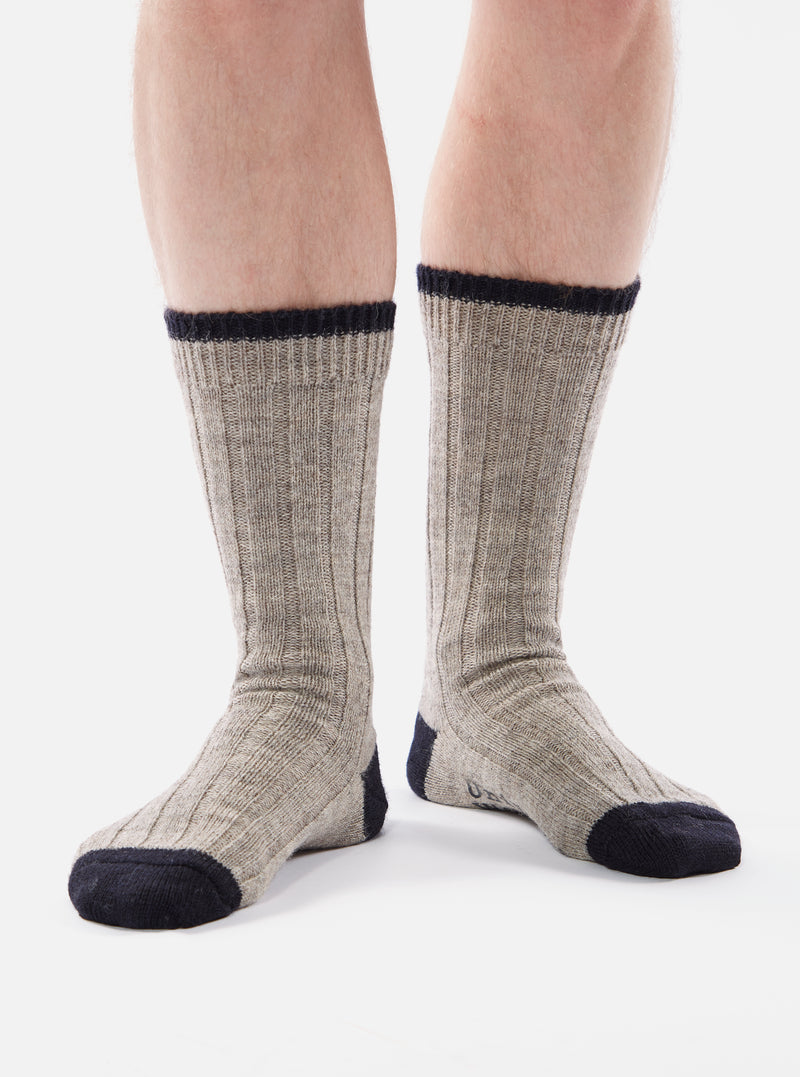 Close-up of a person wearing Stone Wool Hike Sock. The socks are gray with navy blue accents at the toe, heel, and cuff. Ribbed texture. The background is a plain white.