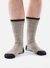 Close-up of a person wearing Stone Wool Hike Sock. The socks are gray with navy blue accents at the toe, heel, and cuff. Ribbed texture. The background is a plain white.
