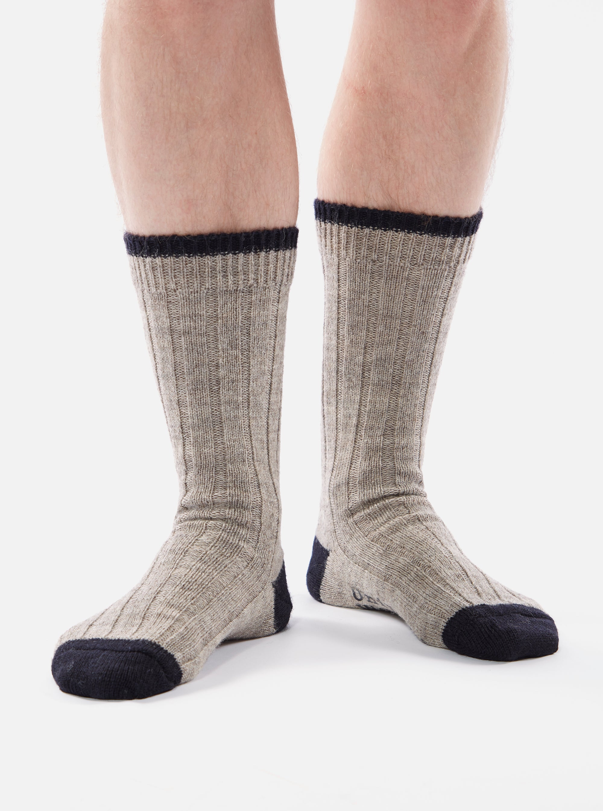 Close-up of a person wearing Stone Wool Hike Sock. The socks are gray with navy blue accents at the toe, heel, and cuff. Ribbed texture. The background is a plain white.