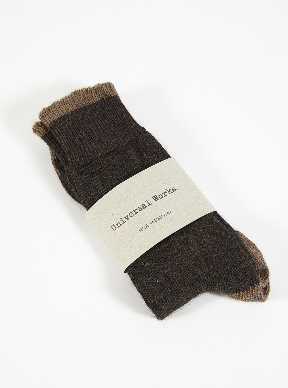 A pair of Charcoal Alpaca Wool Sock on a white surface. The socks are held together by a paper label. The socks are dark brown with a lighter brown trim.