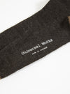 Close up of a Charcoal Alpaca Wool Sock on a white background. The sock is charcoal gray with the brand name "Universal Works" and "made in england" printed on it.