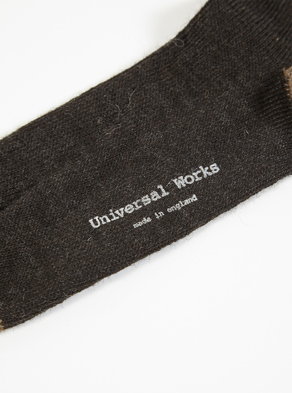 Close up of a Charcoal Alpaca Wool Sock on a white background. The sock is charcoal gray with the brand name "Universal Works" and "made in england" printed on it.