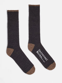 Two Charcoal Alpaca Wool Sock on a white background. The socks are charcoal with brown toes and cuffs. One sock has the words "Universal Works. Made in England" printed on it.