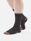 A person stands on a white background wearing Charcoal Alpaca Wool Sock. The sock is charcoal with a brown toe and cuff.