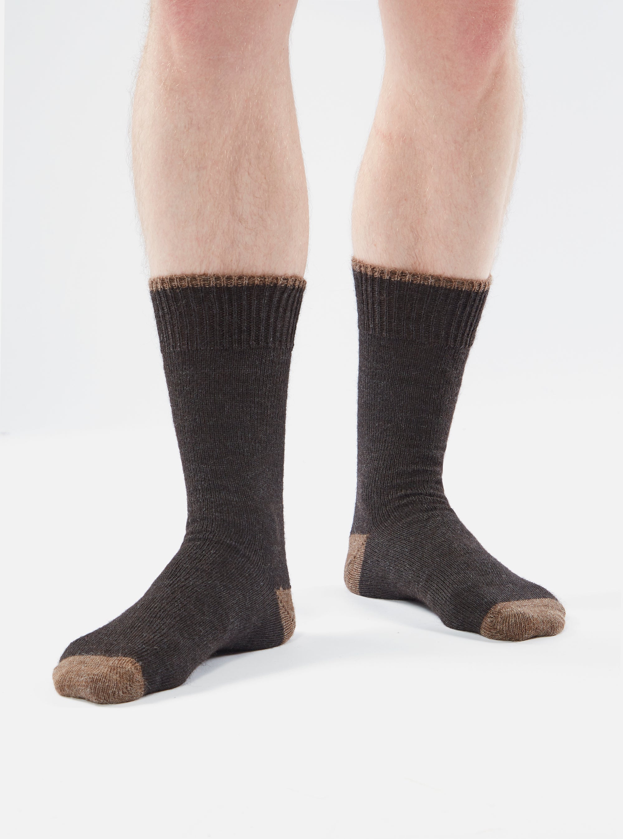 A pair of Charcoal Alpaca Wool Socks are shown on a person against a white background. The socks are charcoal with a brown toe, heel and cuff.