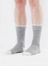 A person wears Grey Marl Alpaca Wool Sock on a white background. The socks are grey with white toes and cuffs.