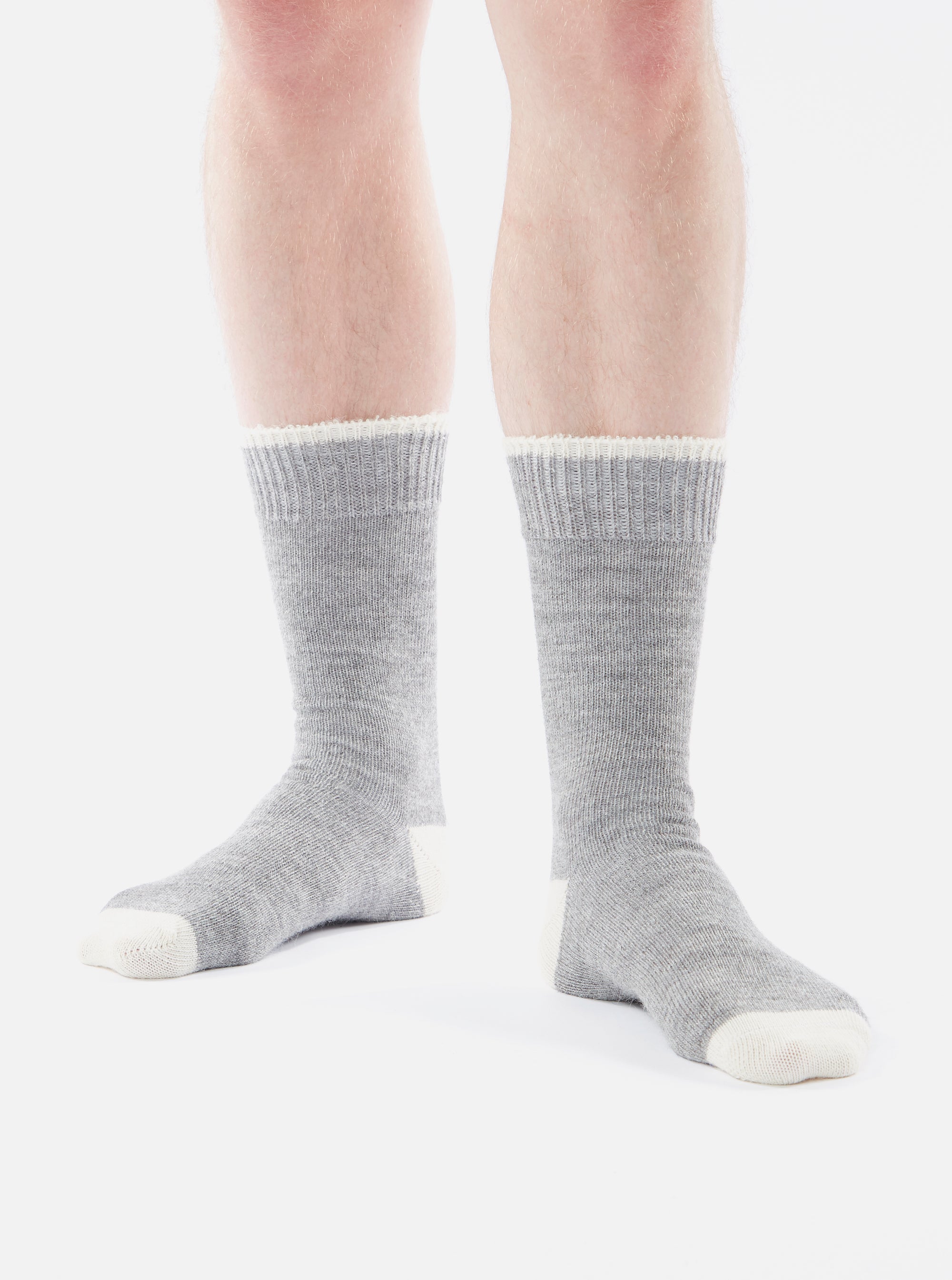 A person stands on a white background wearing Grey Marl Alpaca Wool Sock. The socks are grey with white toes and white trim at the top.