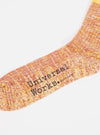 Close-up of a Yellow Cotton Everyday Stripe Sock on a white background. The sock has a striped pattern in yellow, orange, and white. The brand name "Universal Works." is printed on the sock.
