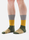 Close-up of a person wearing Grey/Gold Cotton Bold Stripe Sock on a white background. The sock features stripes of grey, gold, green, and tan.