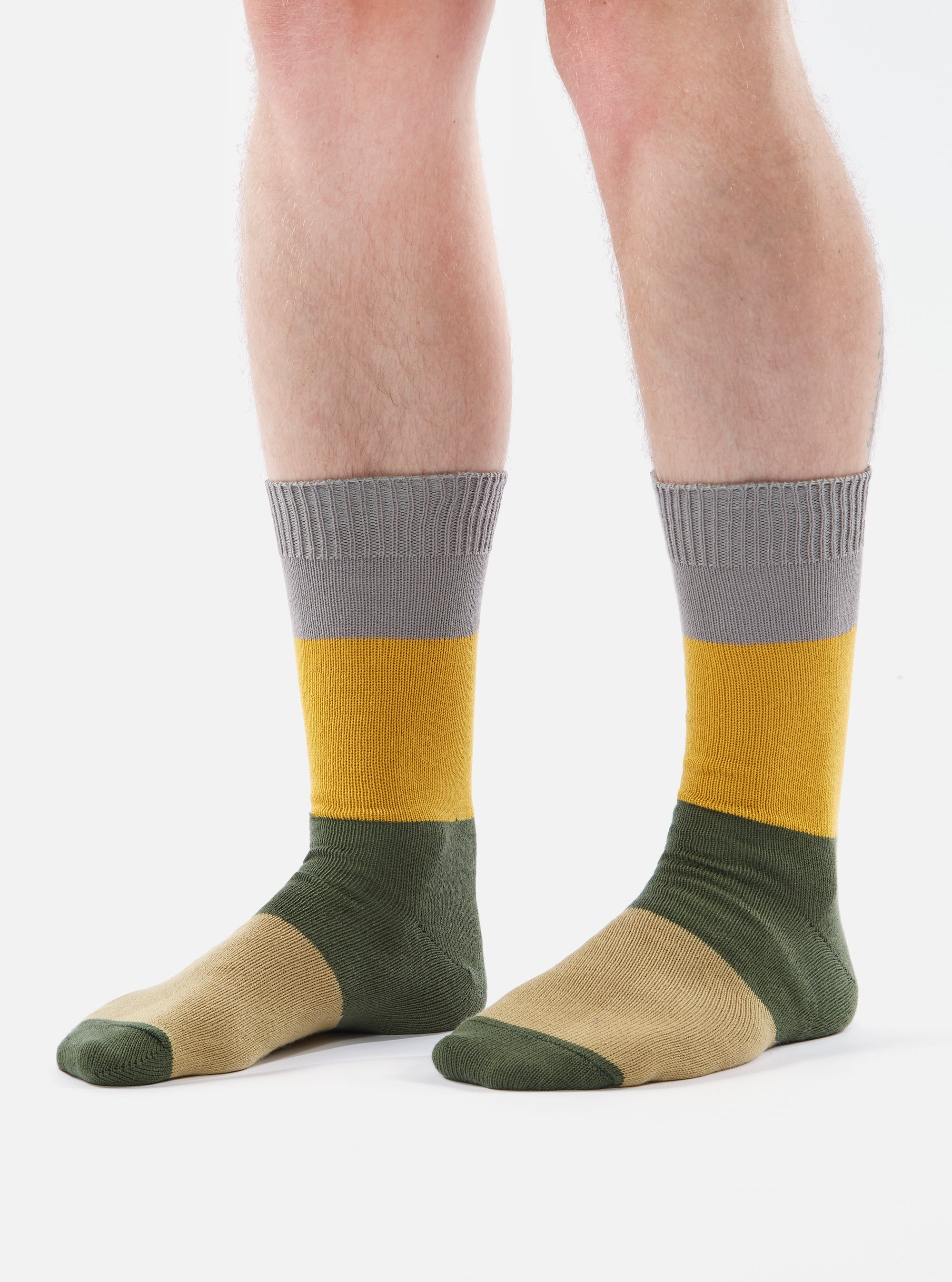 Close-up of a person wearing Grey/Gold Cotton Bold Stripe Sock on a white background. The sock features stripes of grey, gold, green, and tan.