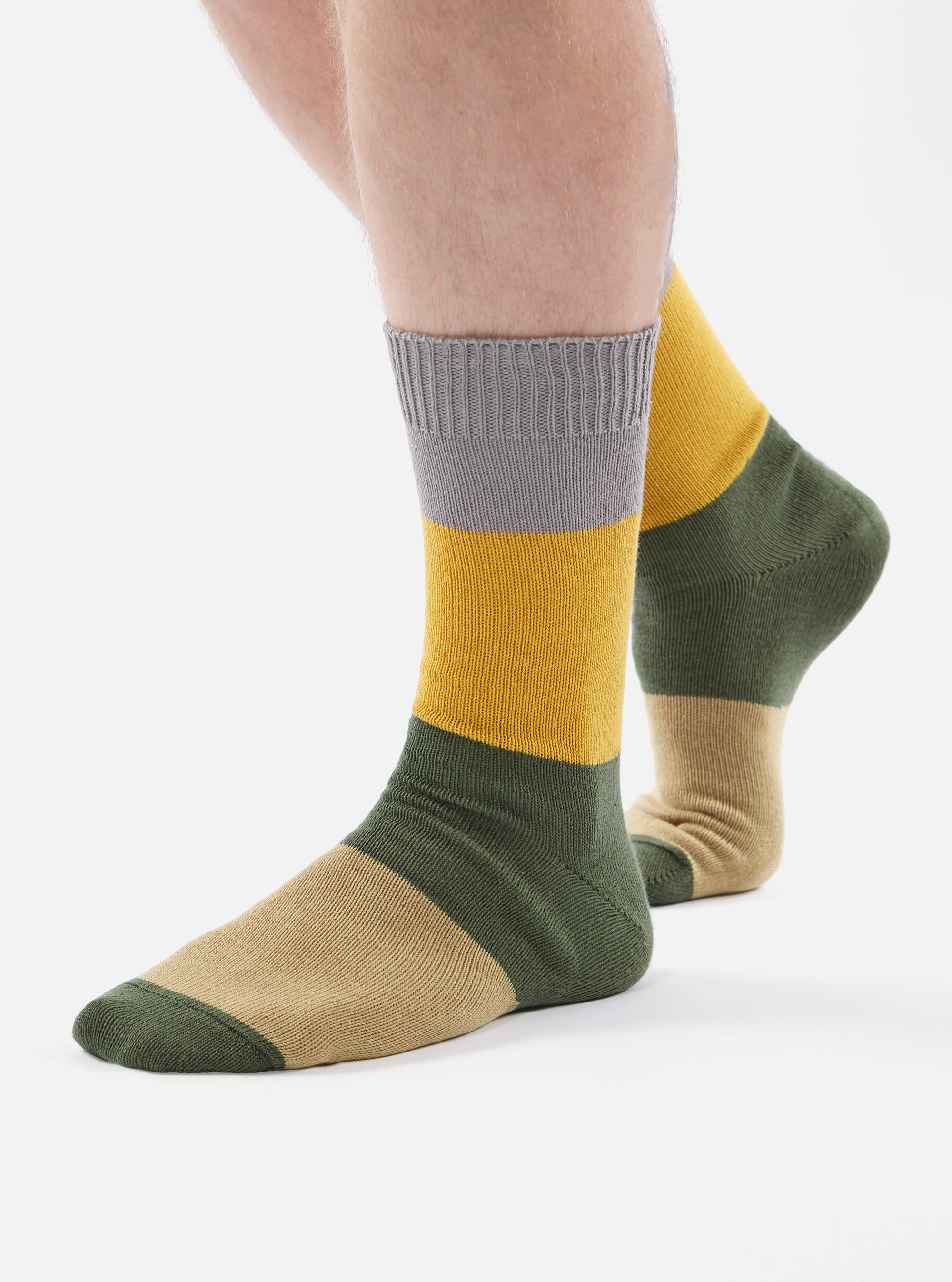 Close-up of a person wearing Grey/Gold Cotton Bold Stripe Sock on a white background. The sock features grey, gold, green, and tan stripes.