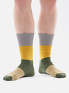 A model wears Grey/Gold Cotton Bold Stripe Sock on a white background. The sock features stripes of grey, gold, olive, and tan.