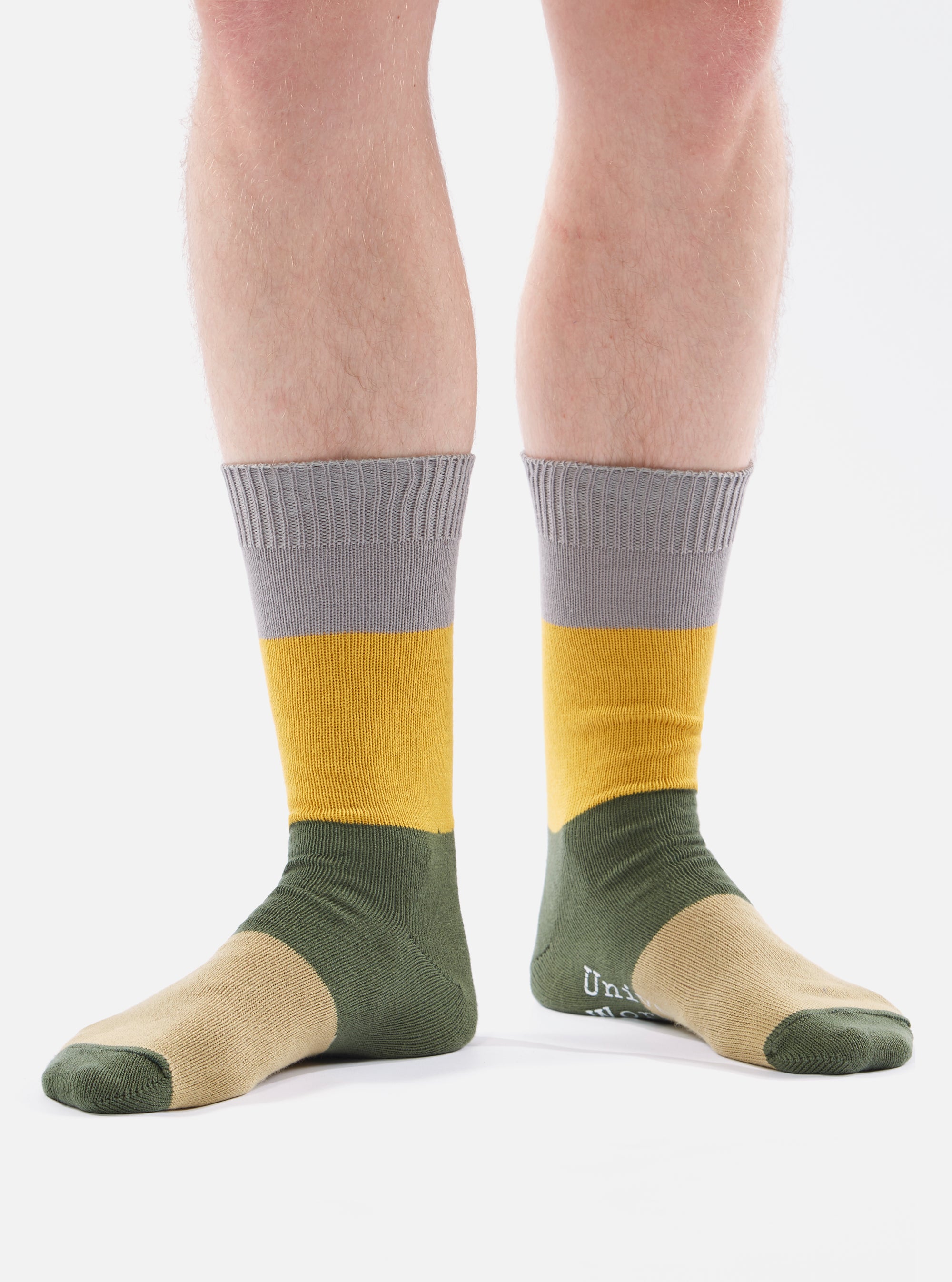 A model wears Grey/Gold Cotton Bold Stripe Sock on a white background. The sock features stripes of grey, gold, olive, and tan.