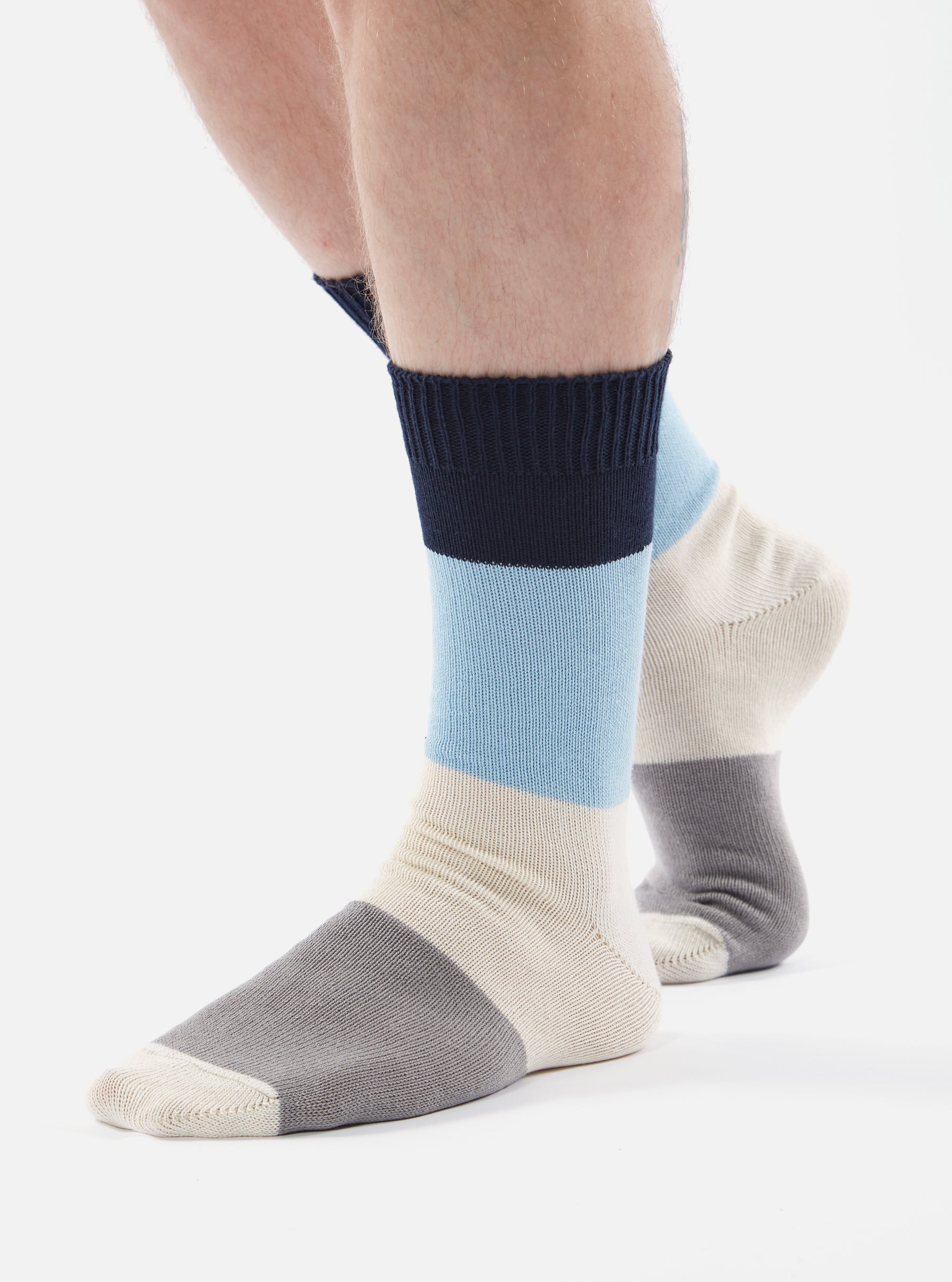 Close-up of a person wearing Navy/Sky Cotton Bold Stripe Sock on a white background. The sock features navy, sky blue, cream, and gray stripes.