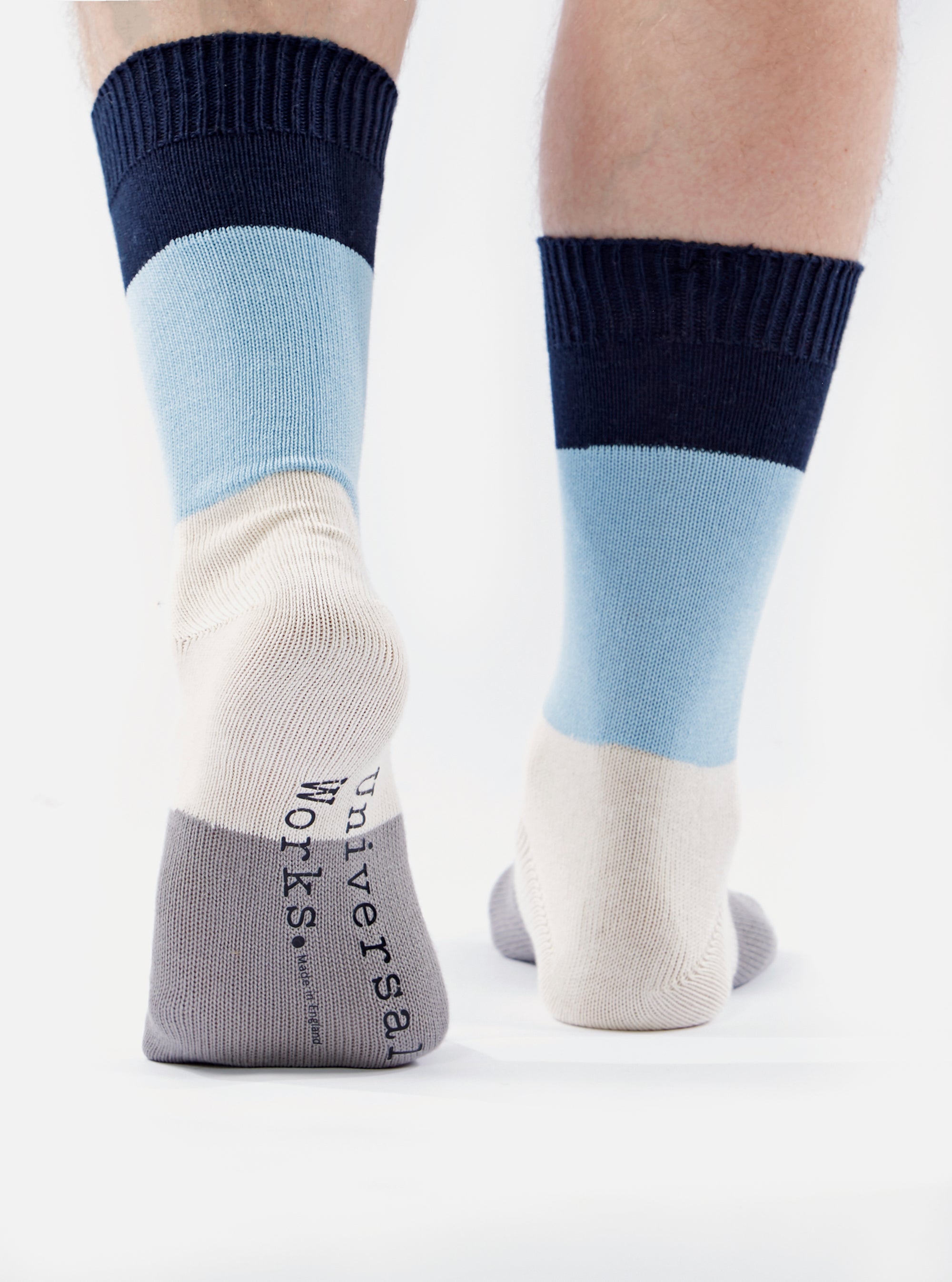 Close-up of a person wearing Navy/Sky Cotton Bold Stripe Sock, showcasing the navy, sky blue, cream, and gray stripes. The socks are cotton and fit snugly. The background is a clean, bright white.