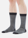 Close-up of a model wearing Grey Marl Merino Classic Sock. The sock is grey with a black toe and top. The background is a plain white.
