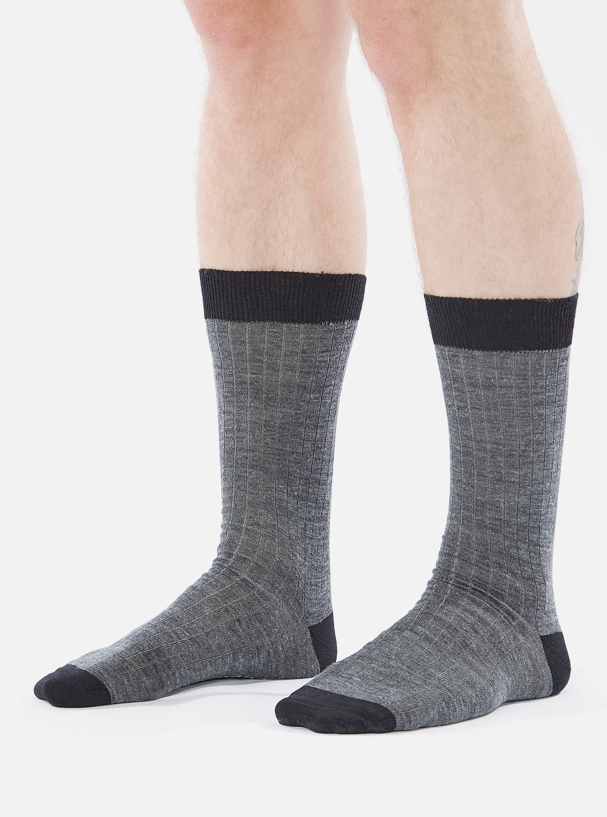 Close-up of a model wearing Grey Marl Merino Classic Sock. The sock is grey with a black toe and top. The background is a plain white.