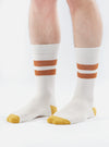Close-up of a model wearing Ecru/Orange Cotton Rib Sport Sock on a white background. The sock features orange stripes and an orange toe.