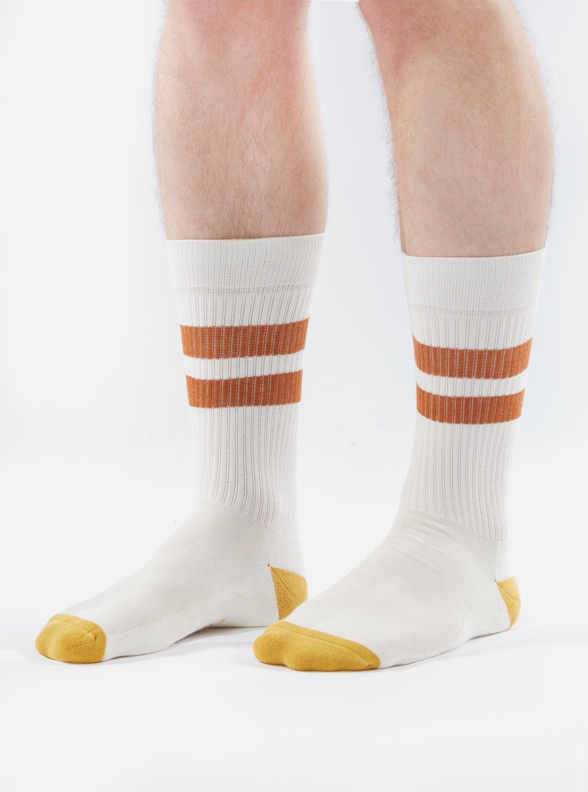 Close-up of a model wearing Ecru/Orange Cotton Rib Sport Sock on a white background. The sock features orange stripes and an orange toe.