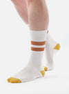 Close-up of a model wearing Ecru/Orange Cotton Rib Sport Sock on a white background. The sock has orange stripes and an orange toe.