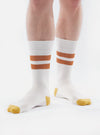 Close-up of a model wearing Ecru/Orange Cotton Rib Sport Sock on a white background. The sock features orange stripes and ecru toe.