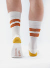 Close-up of a model wearing Ecru/Orange Cotton Rib Sport Sock on a white background. The socks have orange stripes and an ecru heel and toe.