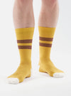 A model wears Yellow/Raisin Cotton Rib Sport Sock, featuring yellow ribbed cotton with raisin stripes and white toes. Shot on a white background.