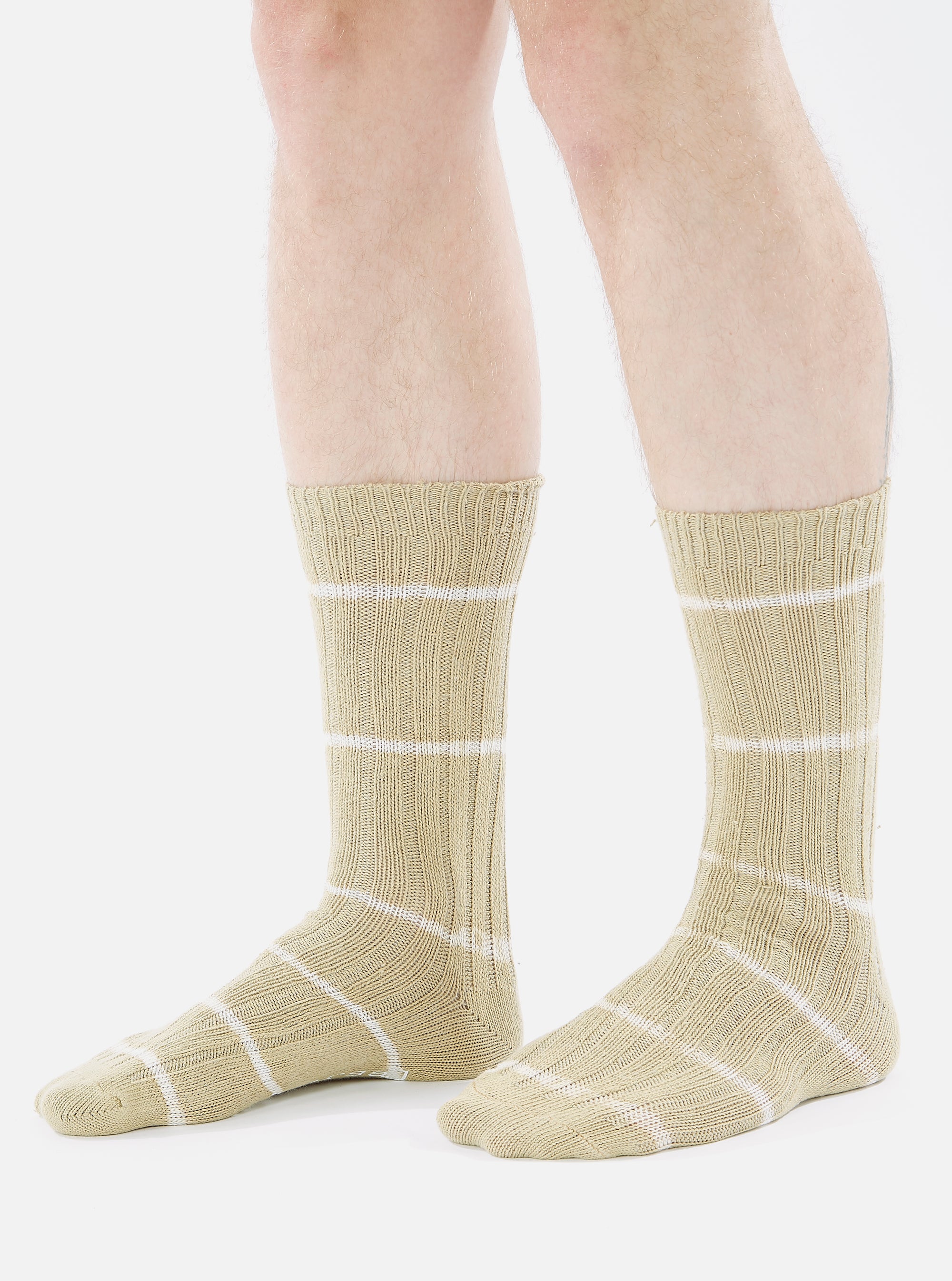 A model wears Dark Sand Tie Dye Knit Slub Socks. The knit socks are tan with white stripes. Shot in a studio with a white background.