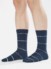 Close-up of a model wearing Navy Tie Dye Knit Slub Sock. The sock is navy with white stripes. The background is a clean white studio setting.
