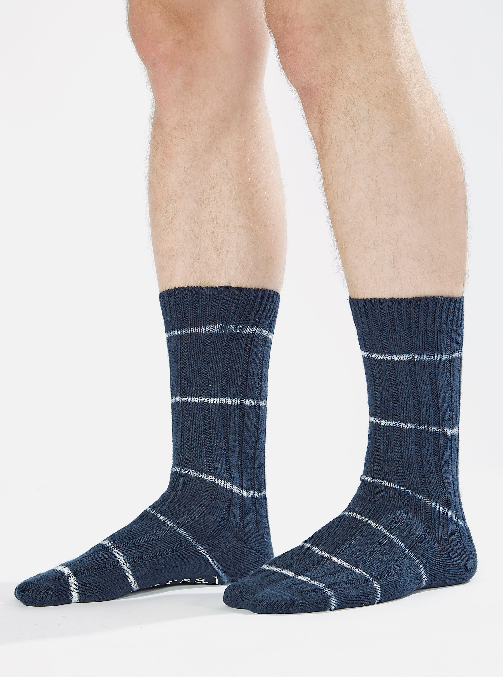 Close-up of a model wearing Navy Tie Dye Knit Slub Sock. The sock is navy with white stripes. The background is a clean white studio setting.