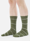 Close-up of a model wearing Olive Tie Dye Knit Slub Sock. The olive green socks have white horizontal stripes. Shot against a white background.