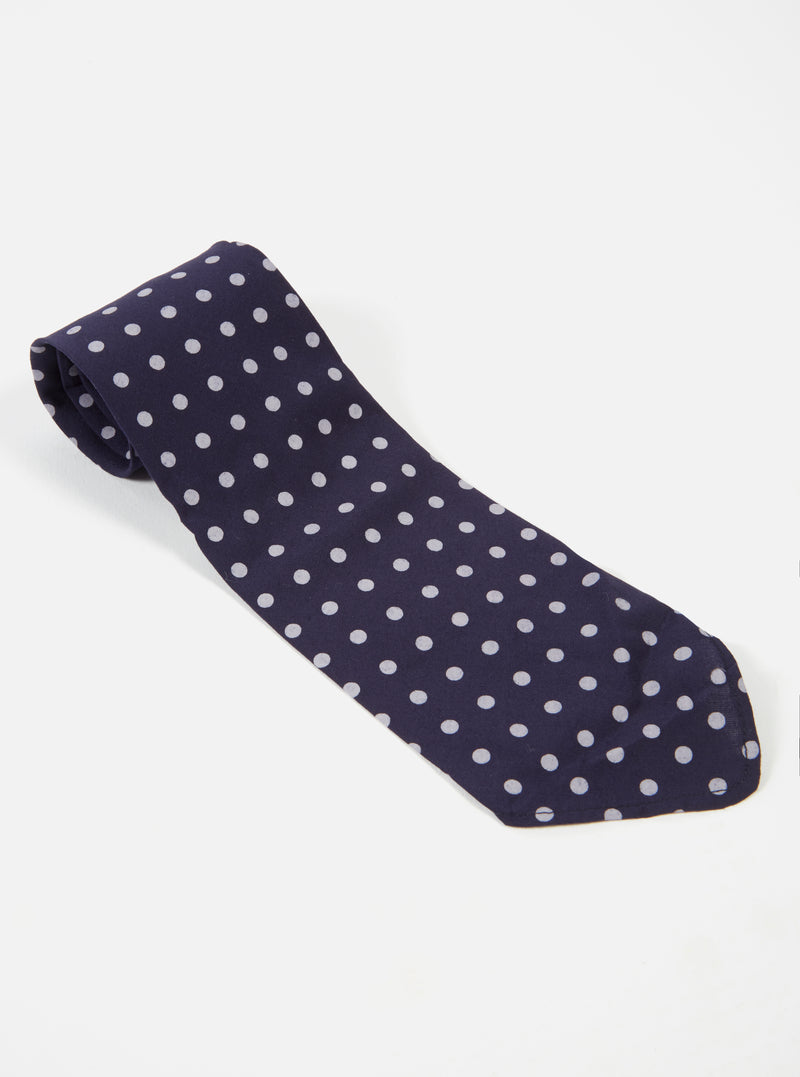 Close-up of a Navy Dot Print Tie on a white surface. The tie is navy blue with white polka dots. The fabric has a smooth, slightly shiny appearance.