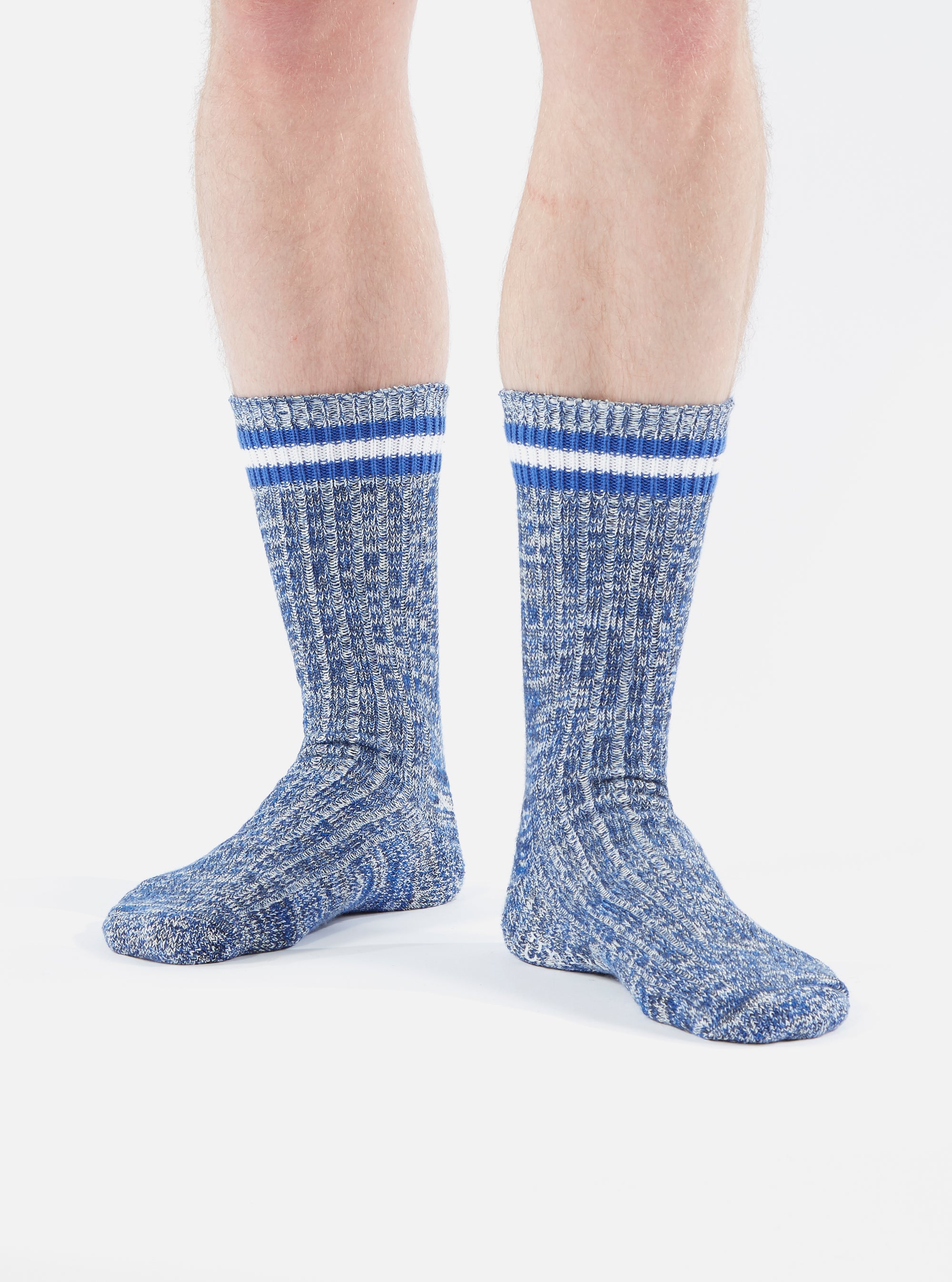 A person stands on a white background wearing the Navy Cotton Everyday Stripe Sock. The sock is a textured navy with white and blue stripes at the top.